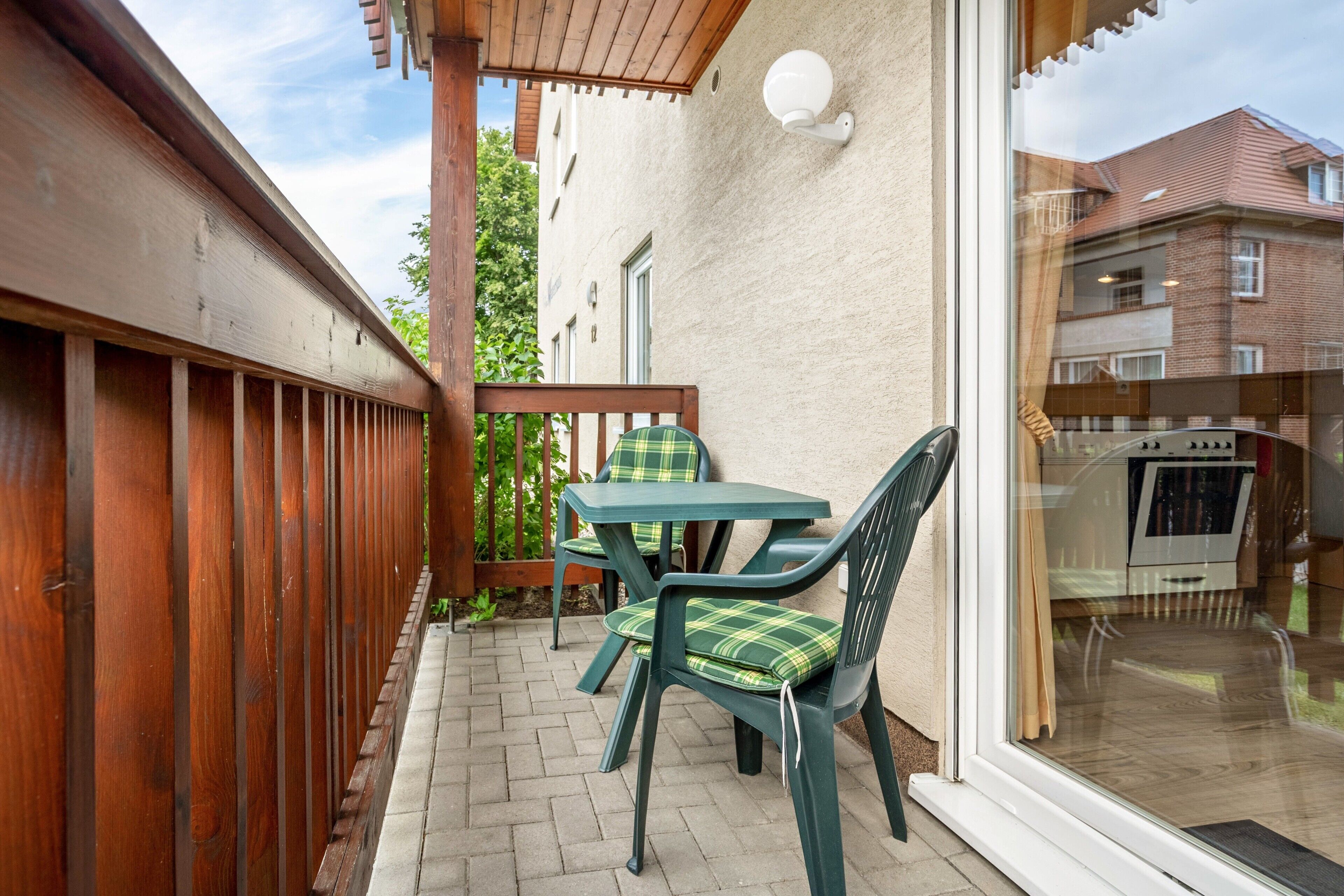 Un patio con barandas de madera, una mesa y dos sillas con cojines verdes.