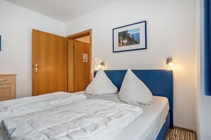 Ett hotellrum med en säng, en trädörr, en inramad tavla på väggen och ett nattduksbord med en lampa.