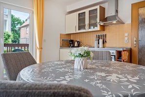 Ein Essbereich mit Tisch, Stühlen, einer Vase mit Blumen und einer Küche im Hintergrund.