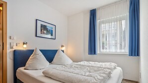 Una habitación de hotel con cama, un cuadro en la pared y una ventana con cortinas.