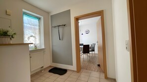 Un pasillo con un radiador, un tapete negro, una ventana con cortina y una puerta que da a un comedor.