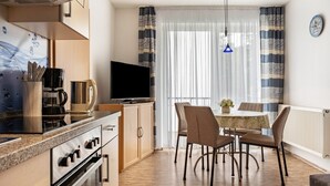 Una cuina moderna amb fogó, forn i cafetera, una zona de menjador amb taula i cadires, i una finestra gran amb cortines.