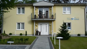A two-story building with a balcony, a door with a handle, and a sign that reads 'Wille Wasserkant'. - Apartment for 2 Guests (55 m²) in Baabe (Baabe)