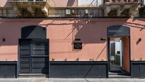 Um edifício com fachada rosa, um portão preto e uma placa indicando 'NAUMACHIA ROOM CENTER'.