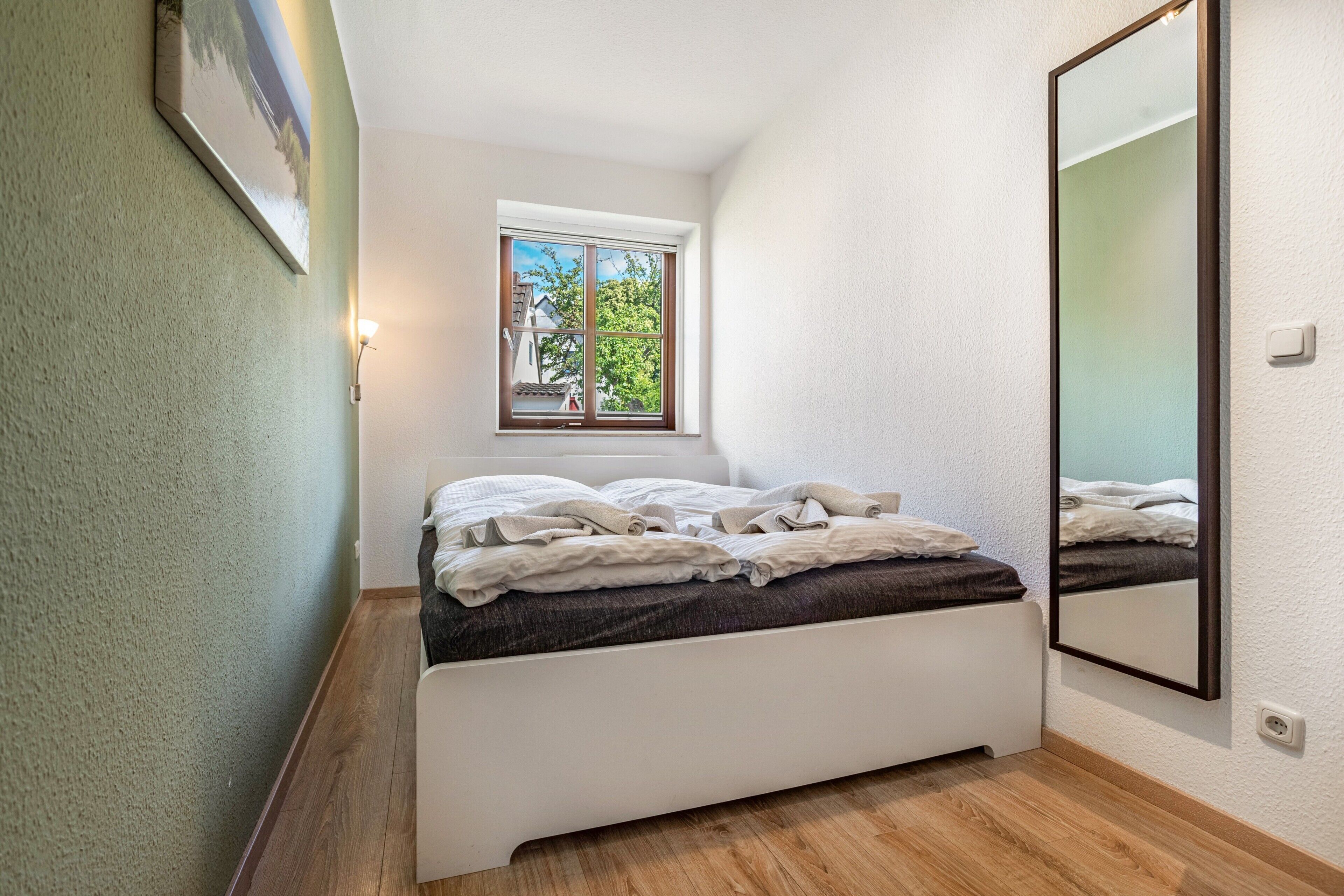 Een slaapkamer met een bed, een raam met uitzicht, een spiegel aan de muur en een lamp.