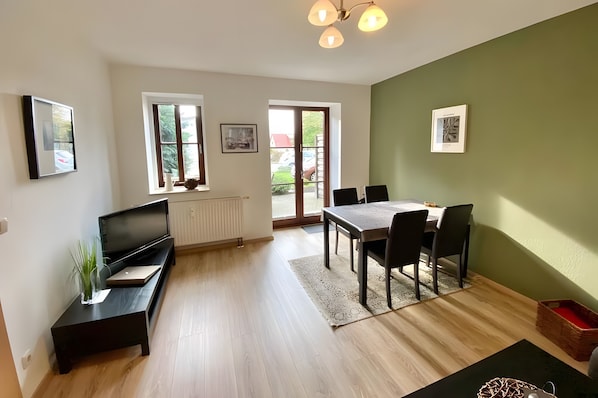 Ein modernes Wohnzimmer mit Sofa, Fernseher, Esstisch und Stühlen.