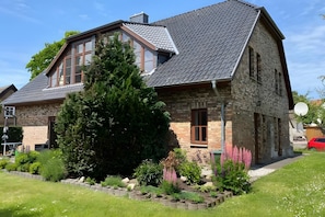 Een woonhuis met twee verdiepingen, een bakstenen gevel, een groot raam en een verzorgde tuin.