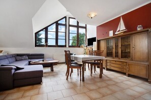 Un vaste espace de vie doté d’une grande fenêtre, d’un canapé de couleur sombre, d’une table à manger avec des chaises et d’un meuble en bois.