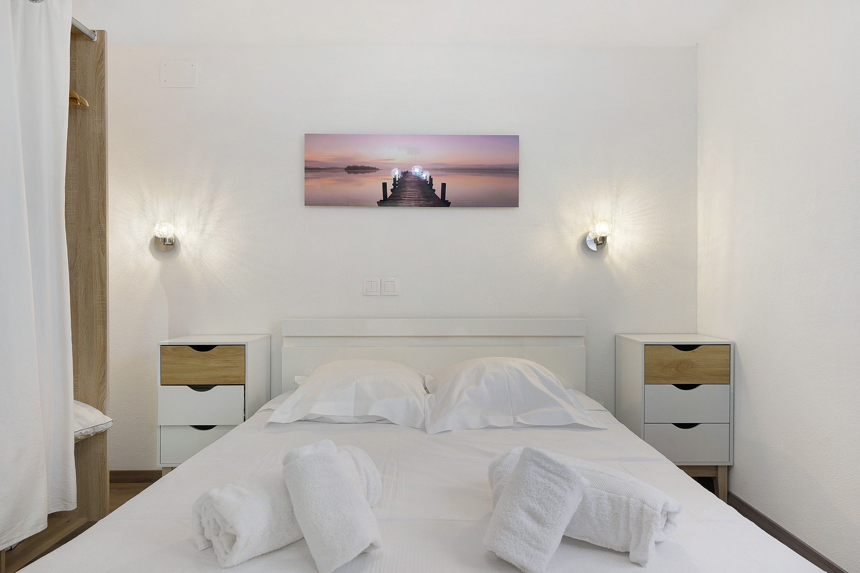 Une chambre d’hôtel avec un lit, deux tables de chevet, un tableau au-dessus du lit et une vue sur une étendue d’eau.