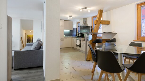 A modern kitchen with a dining area, a sofa, and a staircase.