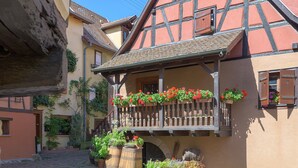 A traditional half-timbered building with a balcony adorned with flowers, a cobblestone street, and a stone barrel.