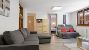 A modern living room with a grey sectional sofa, a grey sofa with red cushions, a glass coffee table, and a wooden floor.