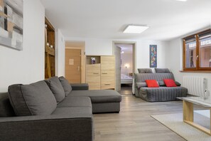 A modern living room with a grey sectional sofa, a grey sofa with red cushions, a glass coffee table, and a wooden floor. - Le Zen d'Eguisheim – A Timeless Escape (Eguisheim)