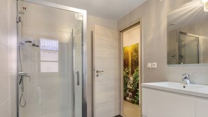 A modern bathroom with a glass shower enclosure, a sink with a mirror, and a door with a nature-themed wallpaper.