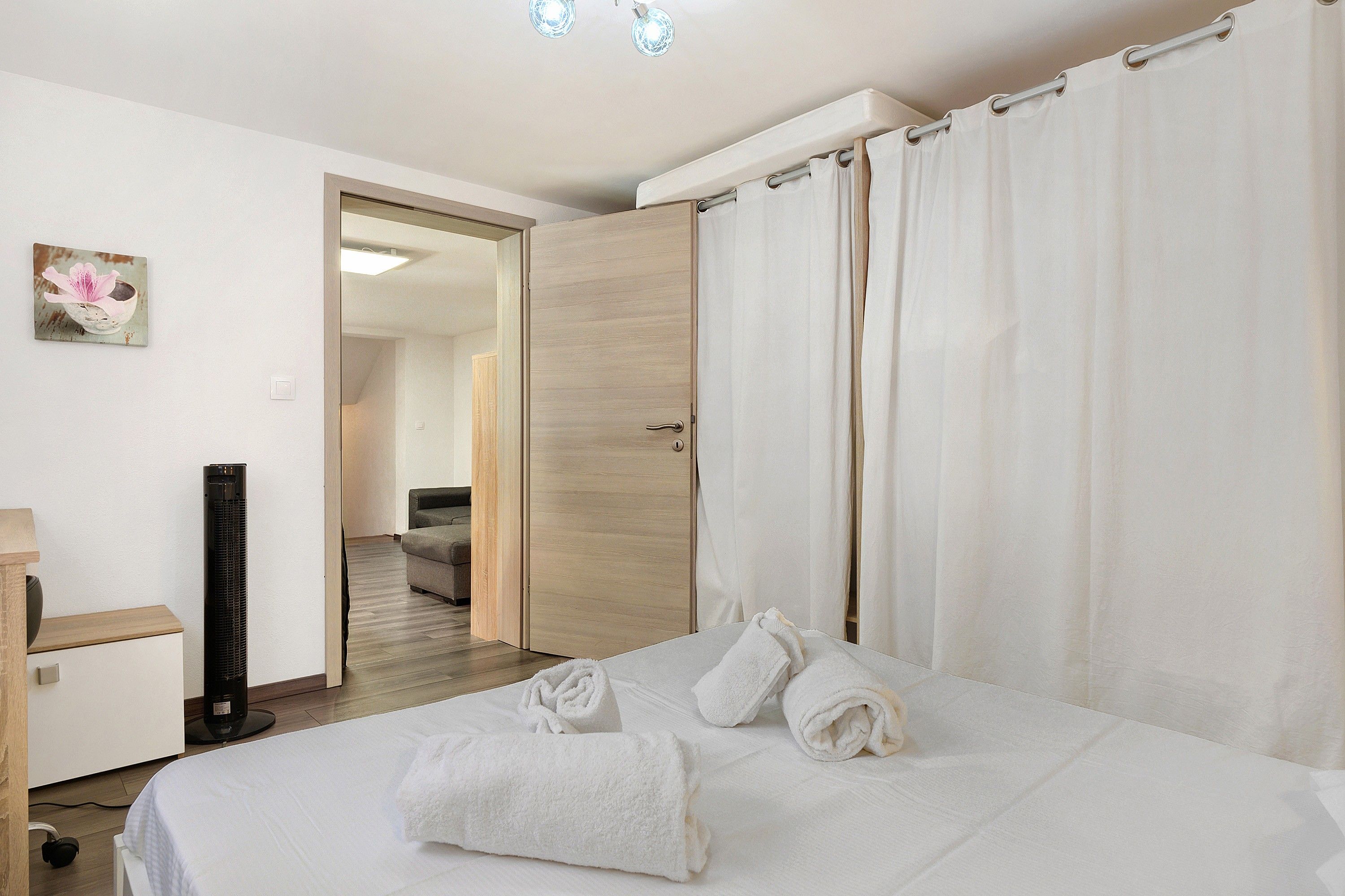 A hotel room with a bed, a flat-screen TV, a wooden door, and a bathroom visible through an open door.