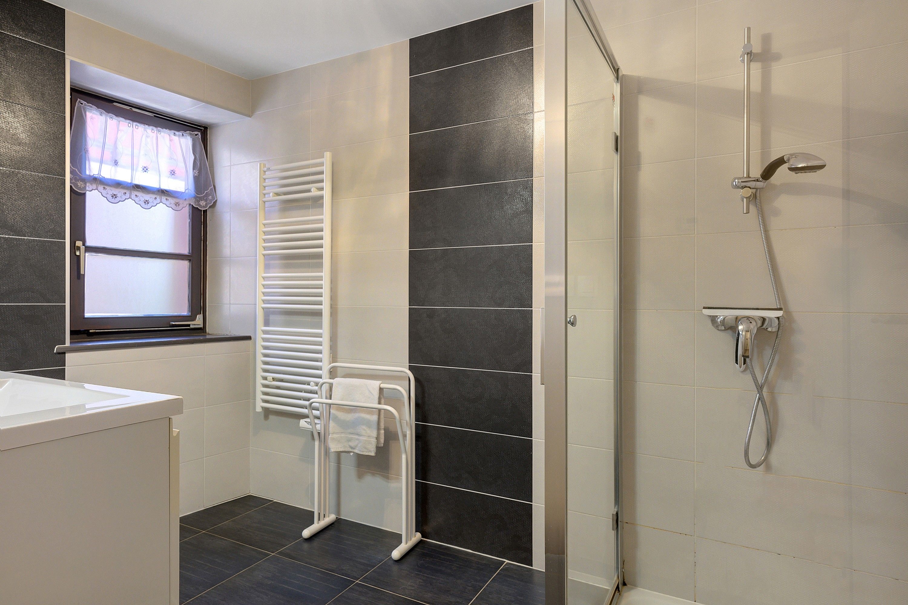 Une salle de bain moderne équipée d’une douche, d’un porte-serviettes et d’une fenêtre avec un rideau.