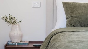 A bedroom with a bed, bedside table, a vase with a plant, and a book titled 'Edible Garden' by Paul West. - 'Eclipse' at Small Batch (Budgee Budgee)