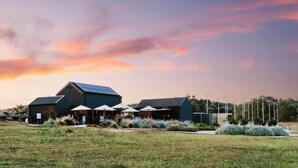 A modern building with a large roof, outdoor seating area, and a grassy field. - 'Eclipse' at Small Batch (Budgee Budgee)