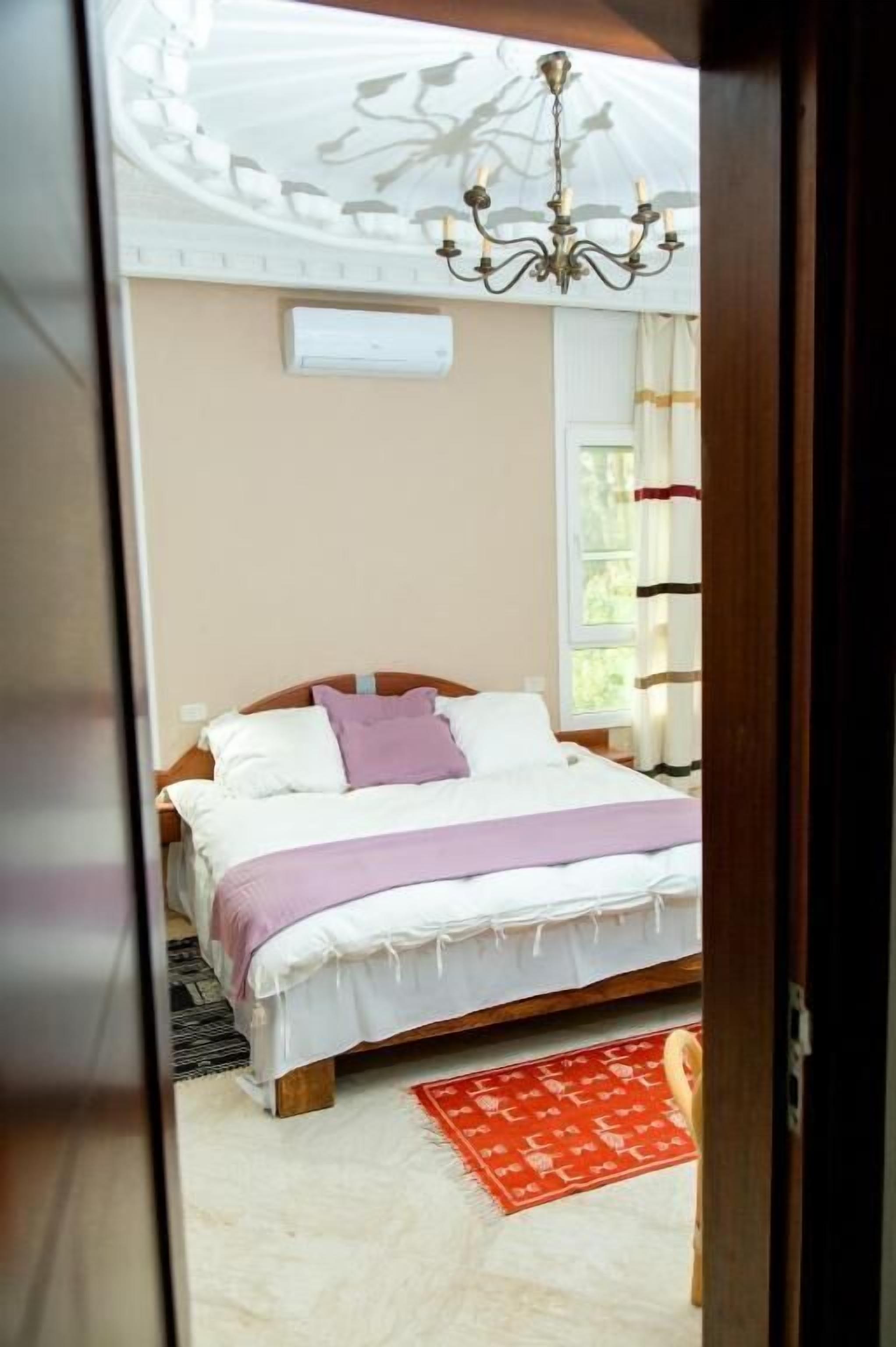 A bedroom with a bed, a chandelier, a window, and a red rug.