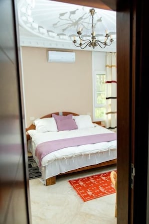 A bedroom with a bed, a chandelier, a window, and a red rug. - Dar Rouissi (Tozeur)