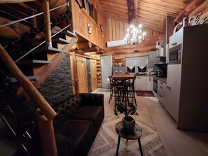 Ein gemütliches Blockhaus-Interieur mit Treppe, Essbereich, Küche und Wohnzimmer mit Sofa und Topfpflanze.