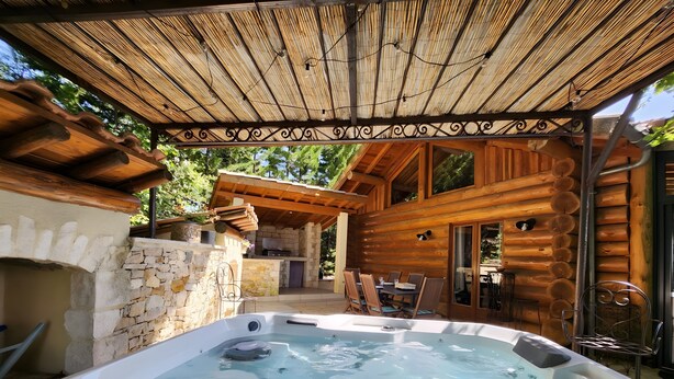 Un jacuzzi en una cabaña de madera con paredes de piedra y una pérgola en la parte superior.