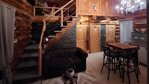 Interior de una cabaña de troncos con escalera, sofá, mesa de comedor y candelabro.