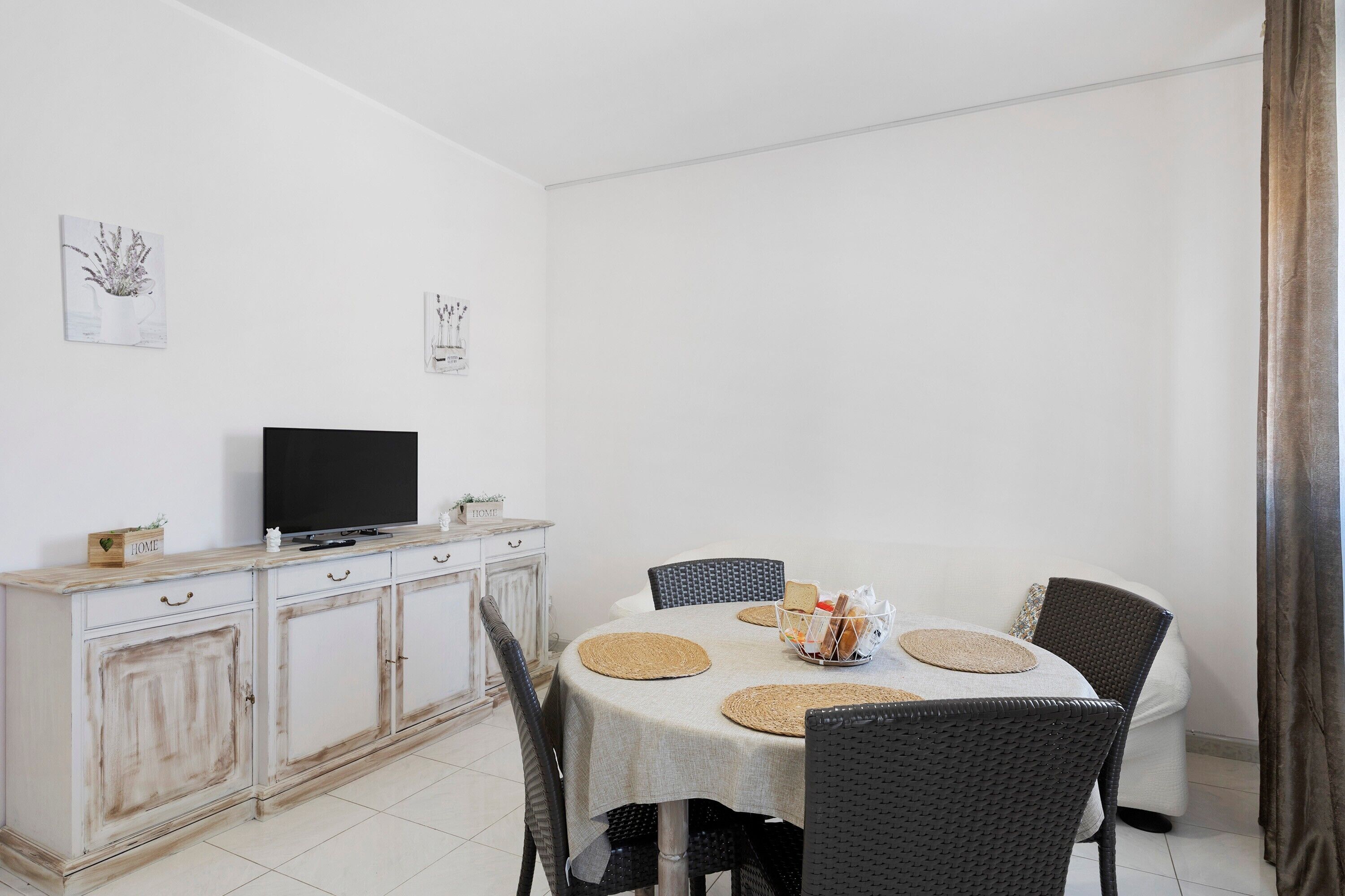 A dining area with a table set for four, a television on a cabinet, and two wall-mounted artworks.
