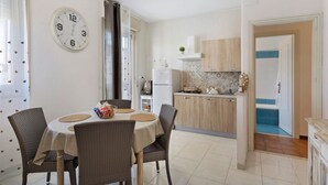 Een eethoek met een ronde tafel, vier stoelen, een klok en een keuken op de achtergrond.