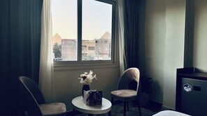 Habitació d'hotel amb una finestra gran, dues cadires, una taula petita amb un vas i un minibar.