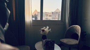 Um quarto com uma janela, um vaso com flores, uma cadeira e uma mesa com uma caixa.