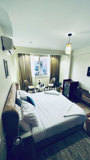 Habitació d'hotel amb un llit, dues cadires, una taula petita amb un vas, escriptori i finestra amb cortines.