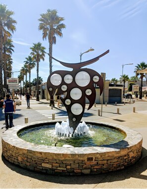 Una plaza pública con una fuente central, palmeras y una escultura distintiva.