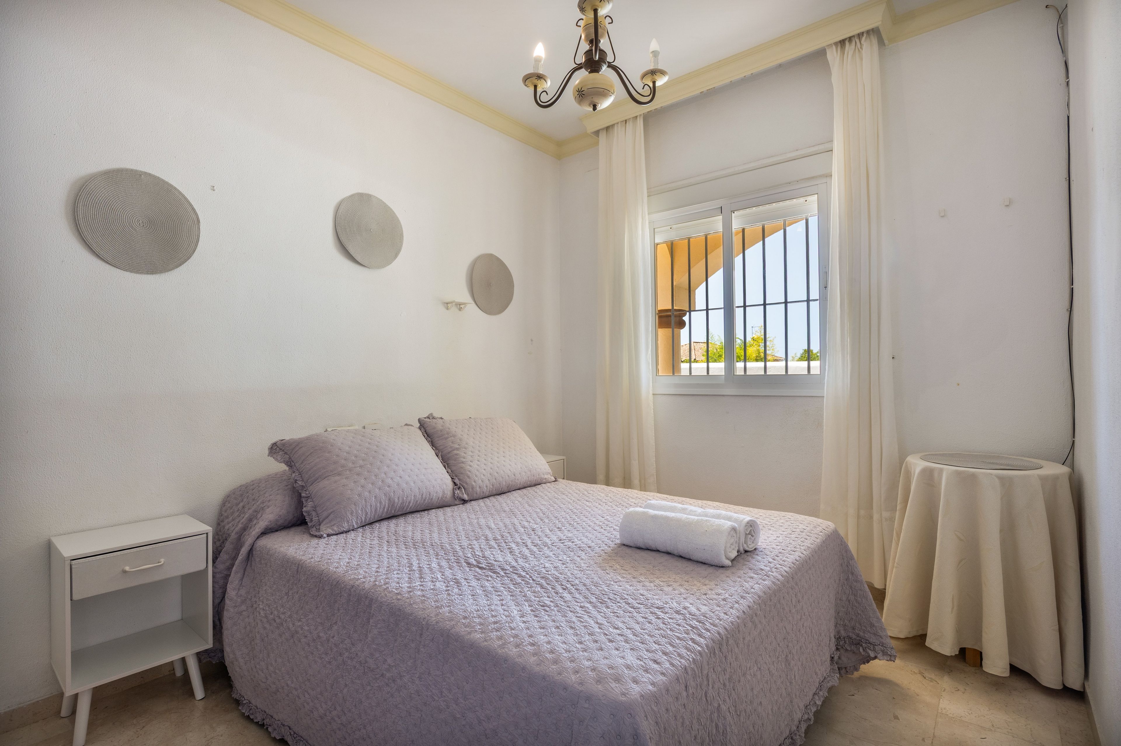 A bedroom with a bed, nightstand, and a window with curtains.