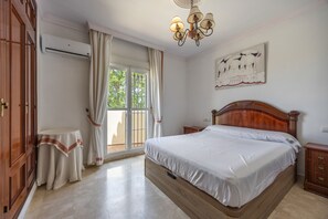 A bedroom with a large bed, a wooden headboard, a nightstand, a bedside table, a wall-mounted air conditioner, and a window with curtains. - Holiday Villa with Private Pool in Chiclana de la Frontera (Chiclana de la Frontera)