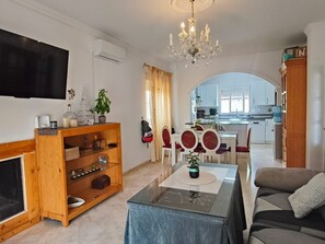 Una sala de estar con televisor, una araña, un sofá y un comedor con mesa y sillas.