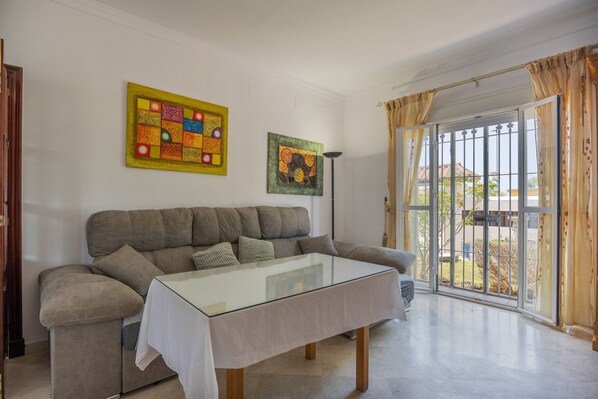 A living room with a sofa, a glass coffee table, and two paintings on the wall.