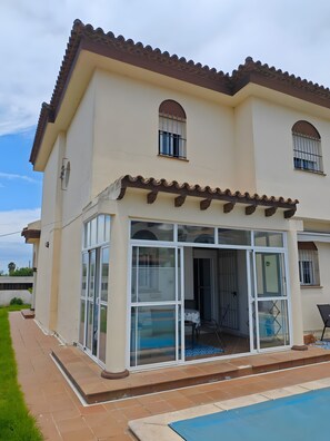 Una casa de dos pisos con un patio, piscina y zona de estar al aire libre techada.