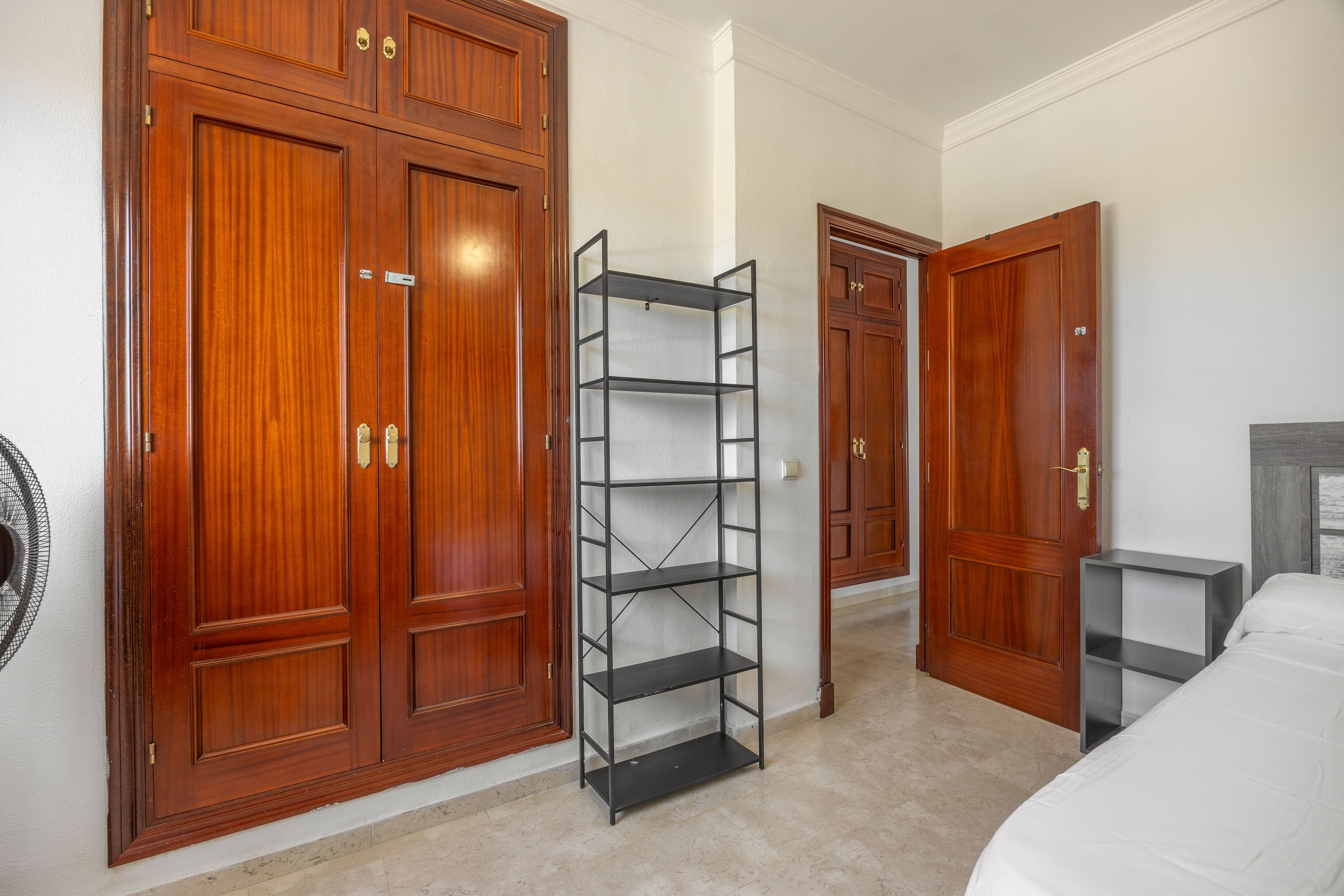 A hotel room with a large wardrobe, a metal shelving unit, and a bed.