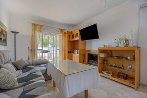 A living room with a sofa, a glass-top coffee table, wooden cabinets, a fireplace, and a flat-screen TV mounted on the wall.