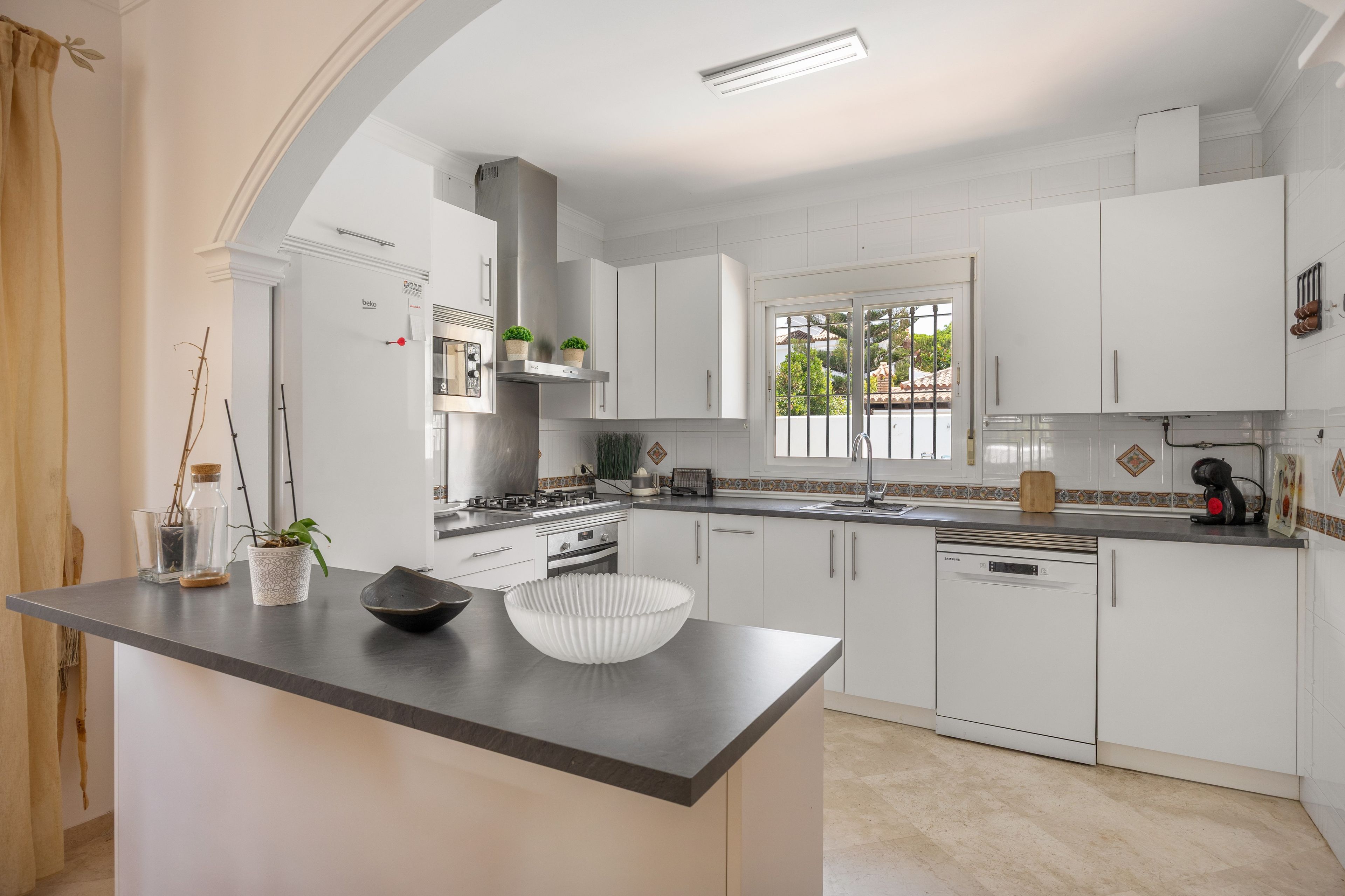 A modern kitchen with white cabinetry, a central island, and a window providing natural light.