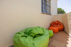 A corner of a building with a tiled floor, a window with metal bars, and two bean bags.