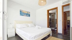 Una camera da letto con un letto, un comodino, un quadro, una zona doccia e una porta che dà su un'altra stanza.