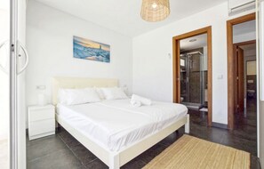 A bedroom with a bed, a nightstand, a painting, a shower area, and a door leading to another room. - Holiday Home 'Kanavayen Tres' with Sea View, Wi-Fi and Air Conditioning (Santanyí)