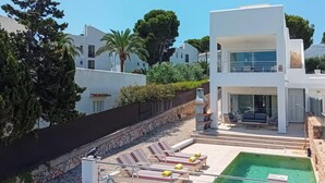 Un edificio moderno de dos pisos con piscina en la azotea, sillas de descanso y una pared de piedra.