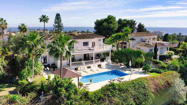Una amplia casa con piscina, rodeada de palmeras y vistas al mar.