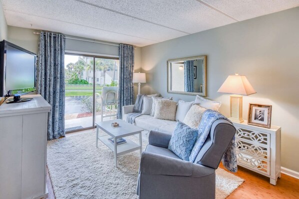 A living room with a sofa, coffee table, TV, and a view of the outdoors. - Ocean and racquet Club: steps to ocean, pool, tennis and pickleball (saint augustine)