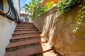 Eine Treppe mit Terrakotta-Fliesen führt zu einem Hauseingang, an einer Seite eine Steinmauer und an der anderen ein Metallgeländer.