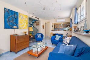 Ein Wohnzimmer mit Sofa, Sesseln, einem Couchtisch, einer Holzkommode und Kunstwerken an den Wänden.