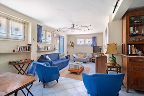 Ein Wohnzimmer mit einer Couch, Sesseln, einem Couchtisch, einer Holzkommode und einem Fernseher.